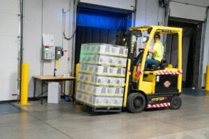 A warehouse employee operating a forklift to move stocked goods indoors. Perfect for industry and logistics visuals.