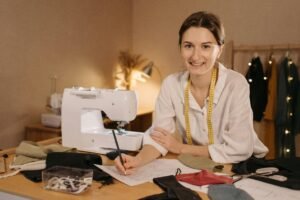 A smiling seamstress working at her table with sewing tools and fabric, promoting a small business atmosphere.